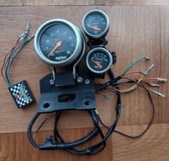 Auto Meter tachometer, voltmeter, and oil temperature gauge set with mounting support for Harley-Davidson motorcycles.