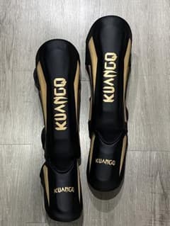 Excellent condition KUANGO leg guards, black/gold, size L, suitable for martial arts and Muay Thai.