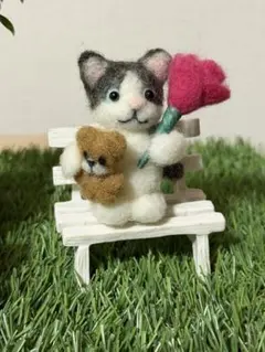 羊毛フェルト♡猫 さんが花とくまのぬいぐるみ を抱っこしています。