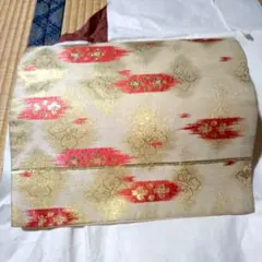 袋帯生成り色地に金銀彩入り赤い横長矢羽根柄似の中に梅桜などの花柄多少の難あり